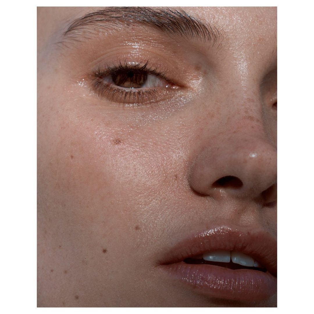 Close-up studio shot of a young adult woman's face, showing her eye, nose, and mouth with glossy lips and highlighted skin.