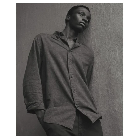 Monochrome portrait of a young African man in a button-down shirt leaning against a wall, eyes looking upward in a contemplative pose.