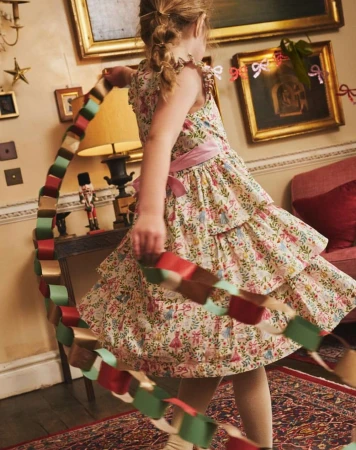A young girl wearing a floral print dress smiles while holding a colorful paper chain in an ornately decorated interior.