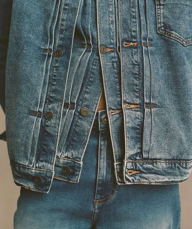 Close-up of a person wearing a matching denim jacket and jeans outfit in a medium shot with neutral lighting and background.