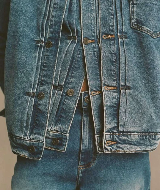 Close-up of a person wearing a matching denim jacket and jeans outfit in a medium shot with neutral lighting and background.