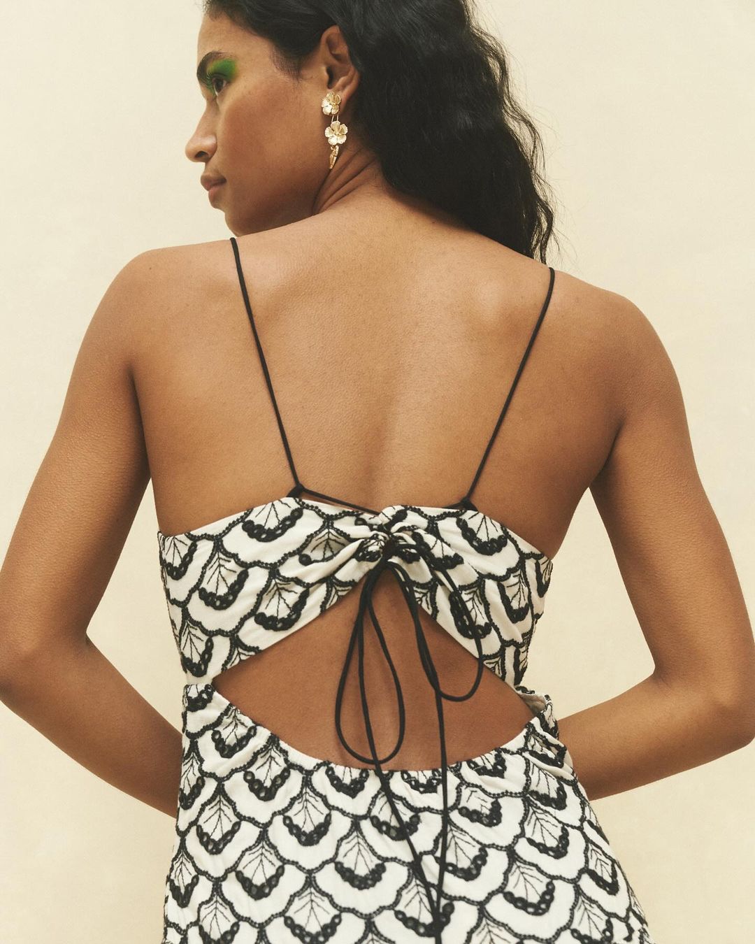 Brunette woman in black and white patterned dress with open back and thin straps, wearing earrings, shot from behind.