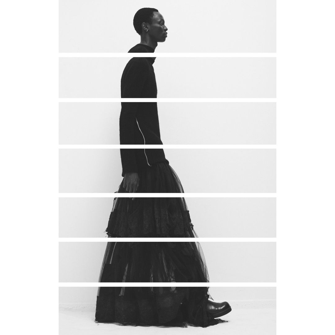 Monochrome studio shot of an adult with short hair in a long black ruffled skirt and top, walking in profile with horizontal lines