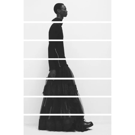 Monochrome studio shot of an adult with short hair in a long black ruffled skirt and top, walking in profile with horizontal lines