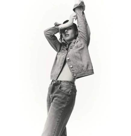 Model in denim jacket and jeans with arms raised against a plain white background by Luke Kuisis