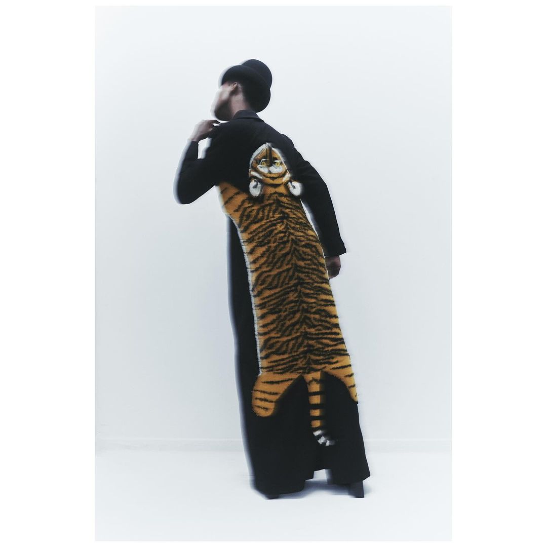 Back view of a person wearing a black coat with a large, vertically-oriented tiger design and head on the back in a light setting.