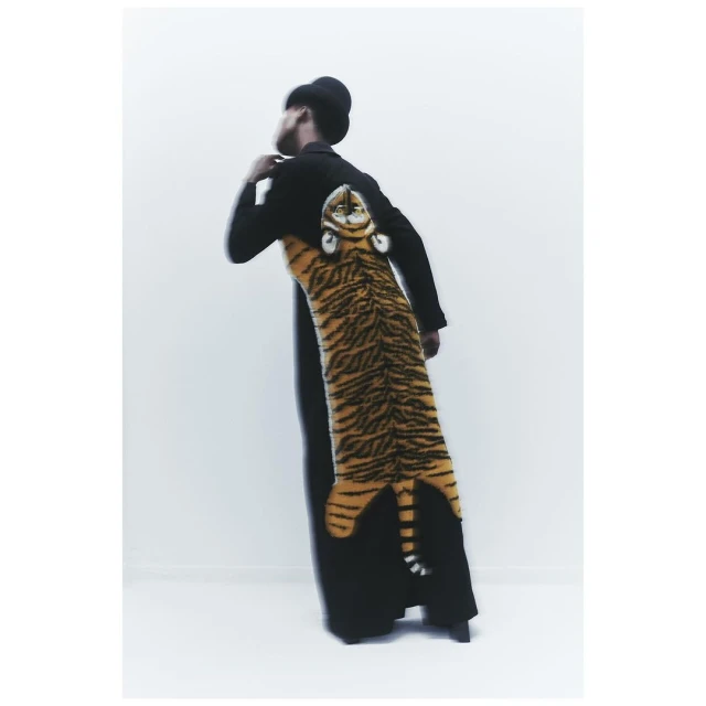 Back view of a person wearing a black coat with a large, vertically-oriented tiger design and head on the back in a light setting.