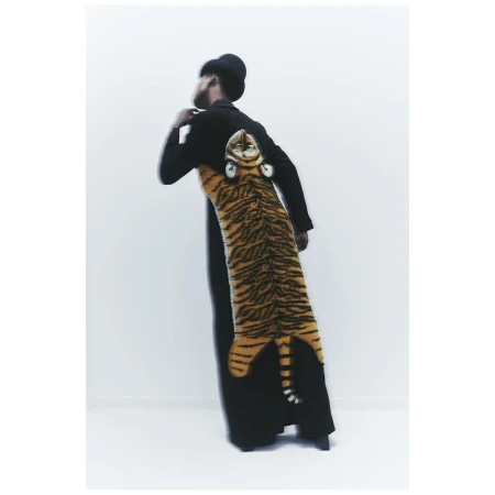 Back view of a person wearing a black coat with a large, vertically-oriented tiger design and head on the back in a light setting.