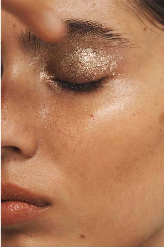 Close-up shot of a woman's face with bronze glitter eyeshadow and glossy skin, emphasizing beauty and makeup artistry.