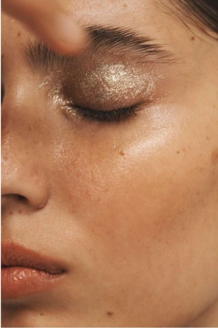 Close-up shot of a woman's face with bronze glitter eyeshadow and glossy skin, emphasizing beauty and makeup artistry.