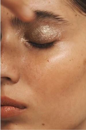 Close-up shot of a woman's face with bronze glitter eyeshadow and glossy skin, emphasizing beauty and makeup artistry.