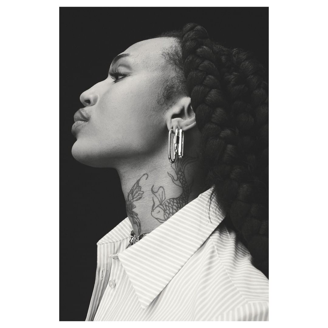 Black and white profile portrait of a woman wearing a striped shirt and large silver earrings with neck tattoos