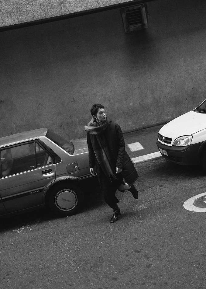 Monochrome street portrait of a person in a dark coat and scarf walking past parked cars in Cape Town by Luke Kuisis.