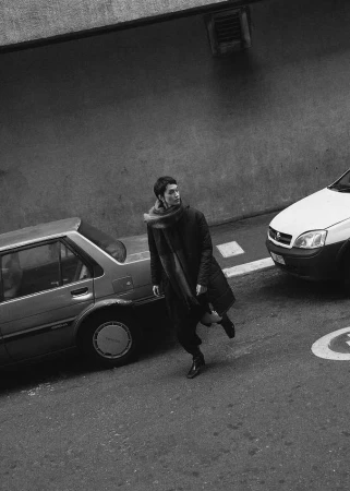 Monochrome street portrait of a person in a dark coat and scarf walking past parked cars in Cape Town by Luke Kuisis.