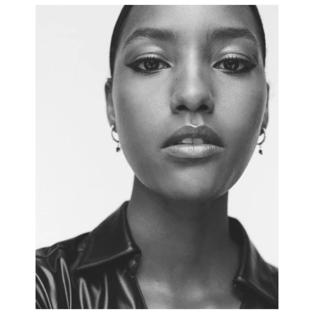 Close-up monochrome portrait of a woman wearing hoop earrings and a dark collar against a plain white background.