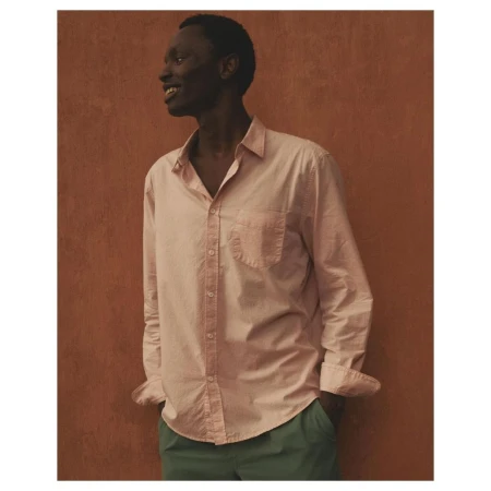 Dark-skinned male model wearing a pink button-down shirt and green trousers poses against a textured orange studio backdrop, smiling.
