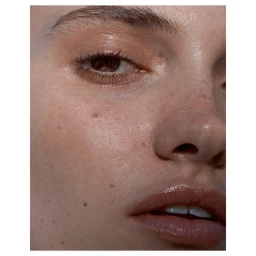 Extreme close up macro beauty portrait of a woman face featuring natural skin texture, glossy lips, and visible freckles.
