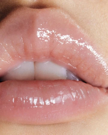 Close-up macro photography of glossy lips with visible texture and two front teeth showing slightly