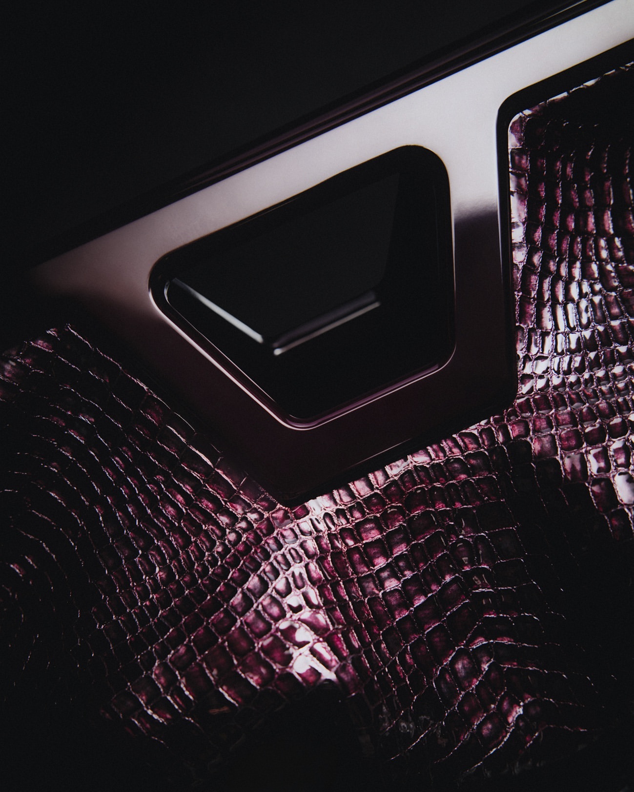 Close-up shot of a car door interior featuring textured crocodile skin and metallic accents on a black background.