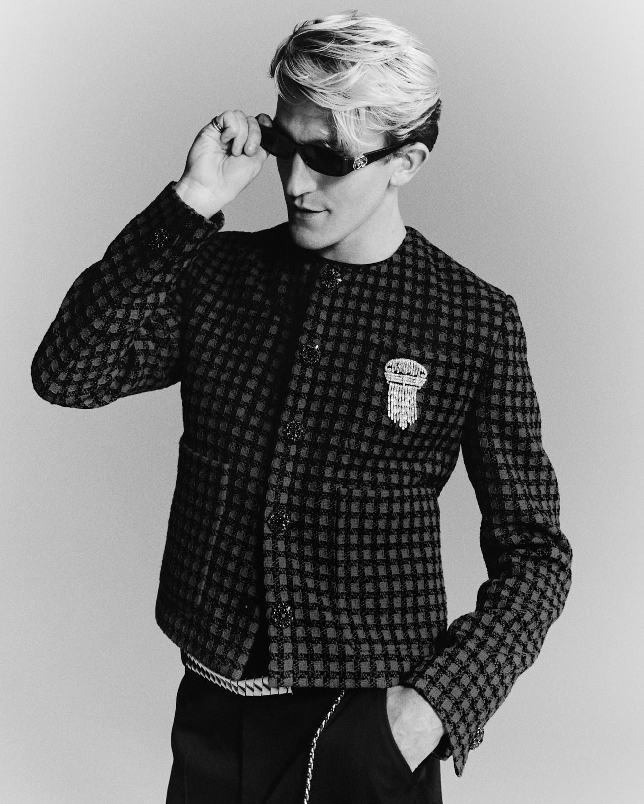Monochrome portrait of a man wearing dark sunglasses and a patterned tweed jacket adjusting his glasses by Lulu Mcardle