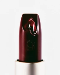 Macro shot of a dark burgundy lipstick with a glossy gel droplet against a plain white background.