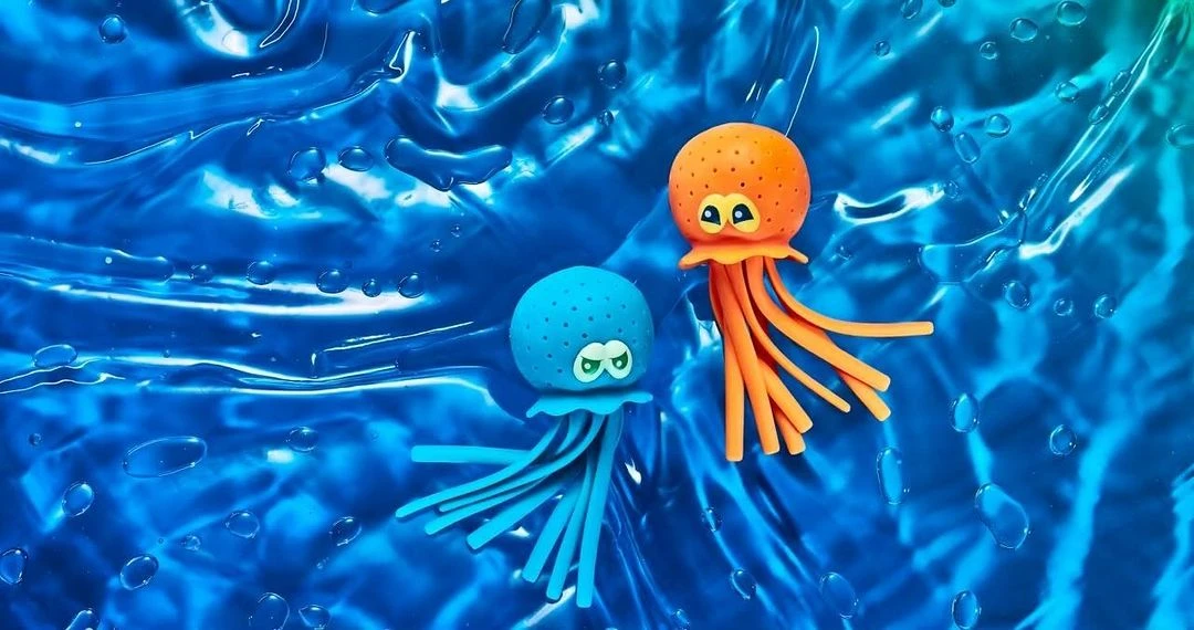 Two animated toy jellyfish, one orange and one blue, sit on a vibrant blue liquid surface, creating a playful and whimsical scene.