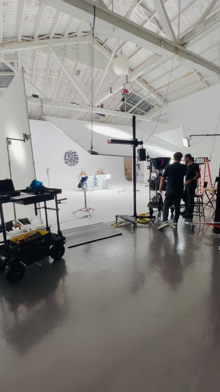 Photo studio interior with two adult men standing near equipment in a white room with lighting and filming setup during daytime.