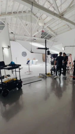 Photo studio interior with two adult men standing near equipment in a white room with lighting and filming setup during daytime.