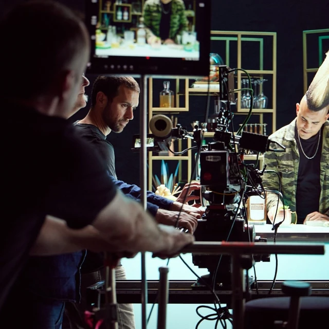 A behind-the-scenes shot of a film or television production, featuring crew members and an actor with a mohawk at a bar setup.