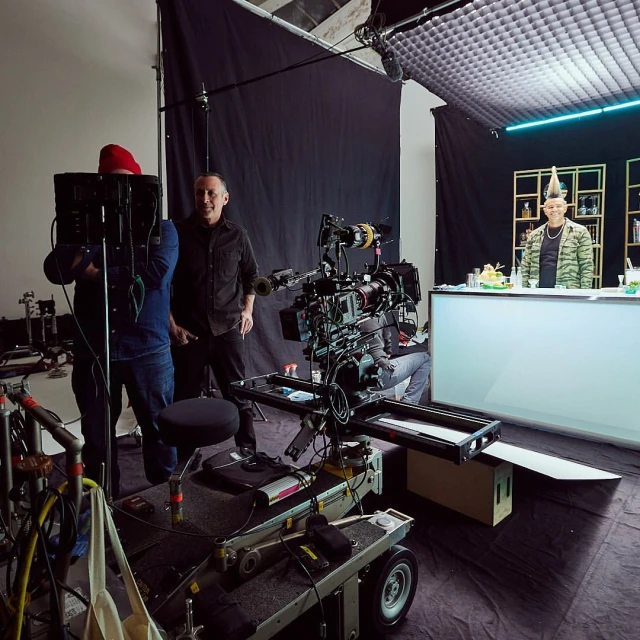 Behind-the-scenes shot of a film set with camera crew, lighting equipment, and a bartender preparing drinks in an indoor photo studio.