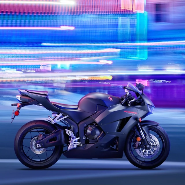 Black Honda CBR600RR motorcycle shown parked on a blue surface against an abstract background of neon blue, pink, and white light trails.