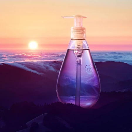 Clear bottle with pump top set against a vivid mountain landscape with a sunrise. Product shot with environmental backdrop.
