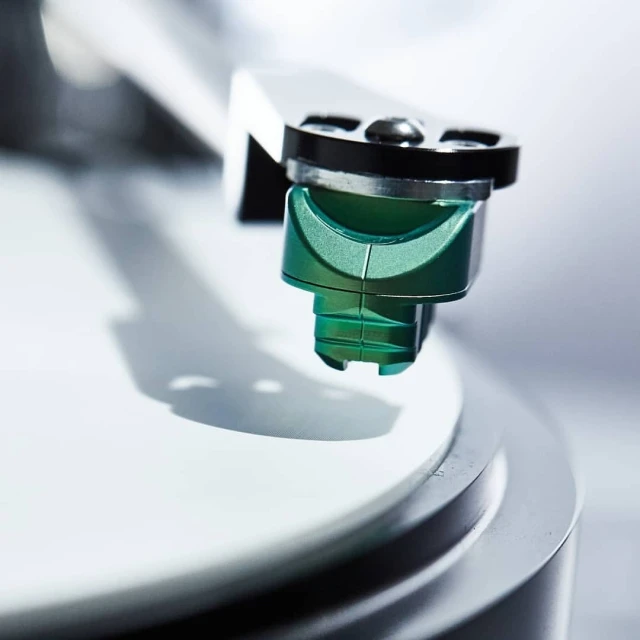 Close-up of a turntable cartridge and stylus, with a sleek, modern design, resting on a white vinyl record.