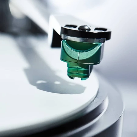 Close-up of a turntable cartridge and stylus, with a sleek, modern design, resting on a white vinyl record.