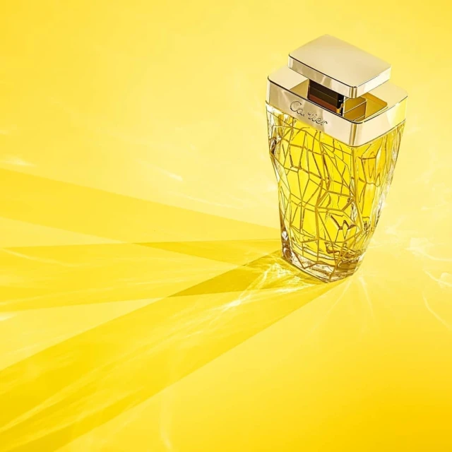 Crystal perfume bottle with gold accents on a sunny yellow background, casting shadows, creating a bright and luxurious aesthetic.