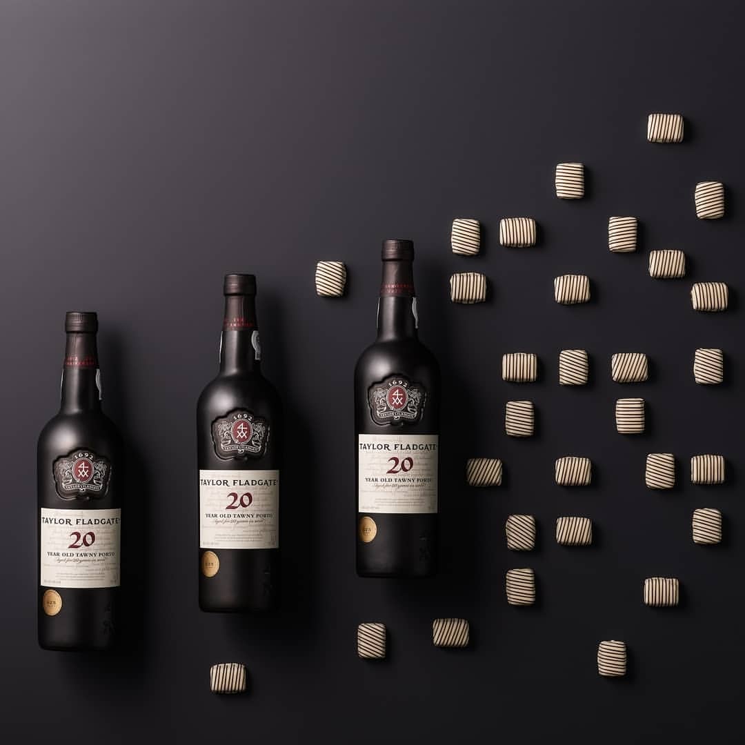 Three bottles of Taylor Fladgate 20-year-old Tawny Port wine surrounded by chocolates on a dark background, product photography.
