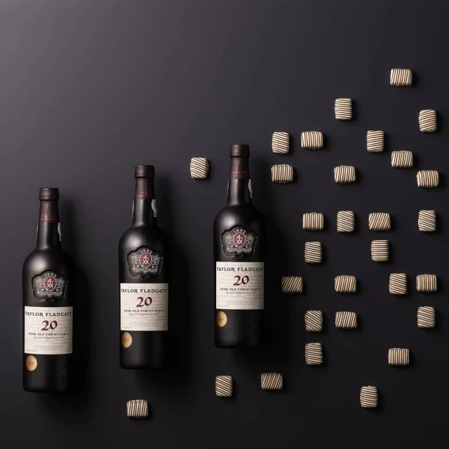 Three bottles of Taylor Fladgate 20-year-old Tawny Port wine surrounded by chocolates on a dark background, product photography.