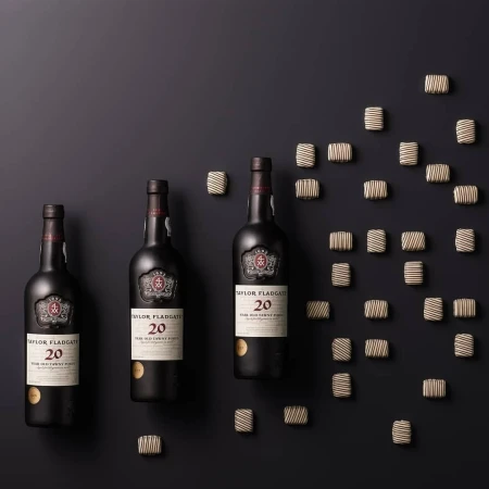 Three bottles of Taylor Fladgate 20-year-old Tawny Port wine surrounded by chocolates on a dark background, product photography.