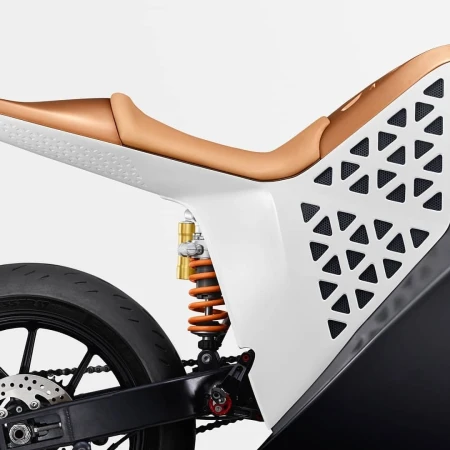Close-up of a modern motorcycle featuring a white and tan frame, black tire, and orange shock absorber against a light background.