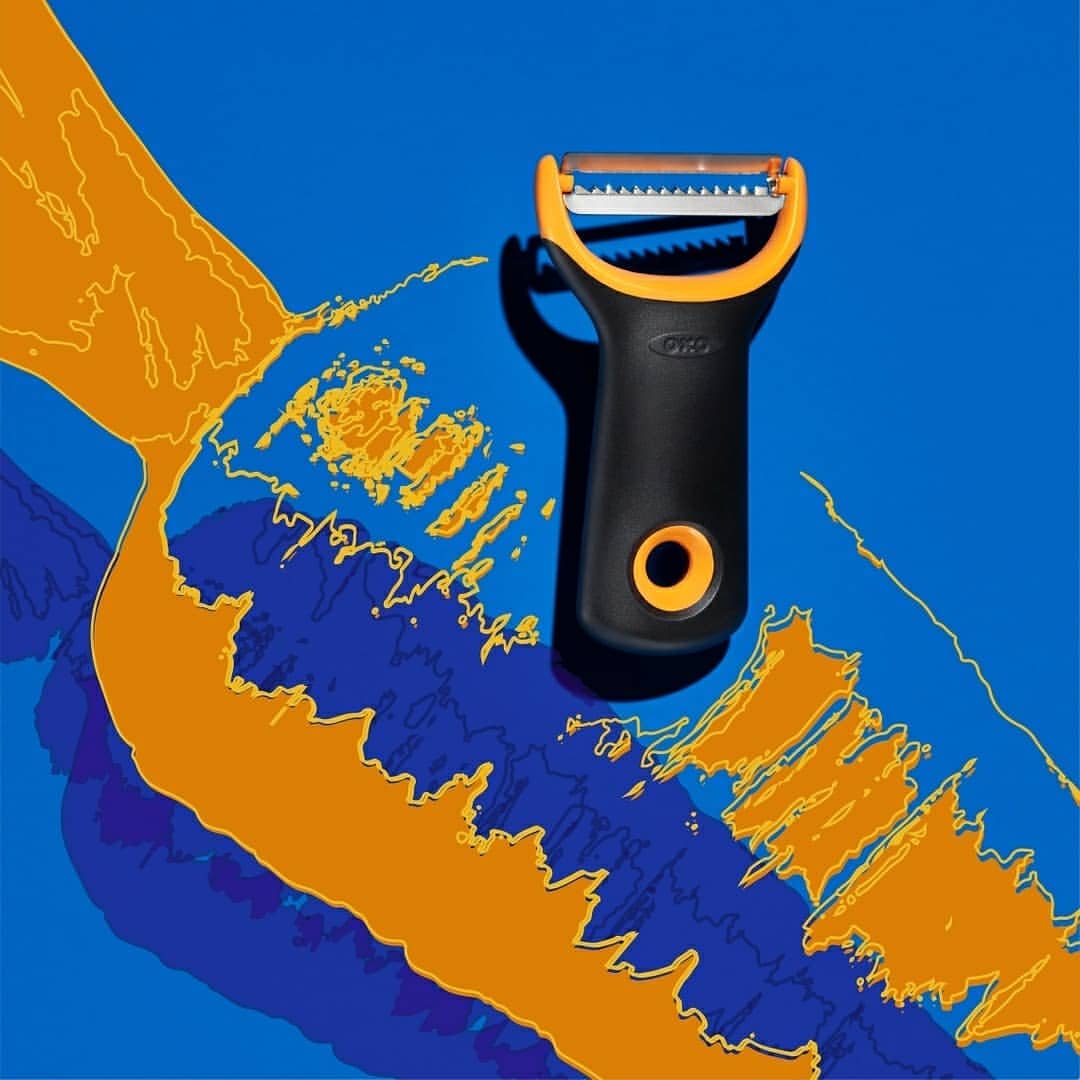 Studio shot of a black OXO peeler with a yellow blade holder on a blue background with abstract yellow and dark blue shapes.