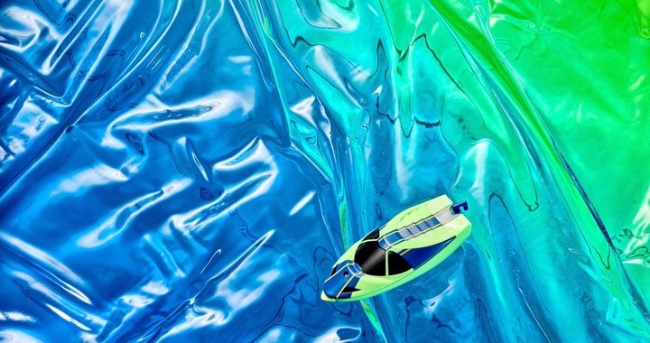 Boat toy on crinkled cellophane with blue, green, and turquoise colors, creating a visually appealing and abstract composition.