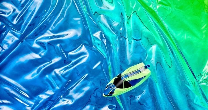 Boat toy on crinkled cellophane with blue, green, and turquoise colors, creating a visually appealing and abstract composition.