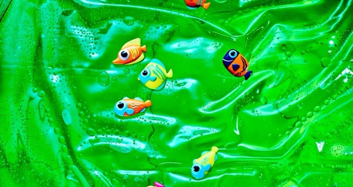Animated cartoon fish swim in a bright green liquid with bubbles creating an underwater effect with vibrant colors and whimsical details.