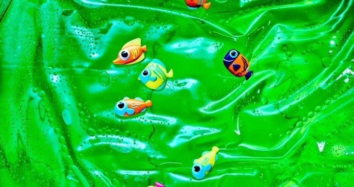 Animated cartoon fish swim in a bright green liquid with bubbles creating an underwater effect with vibrant colors and whimsical details.