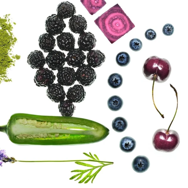 Overhead view of blackberries, blueberries, cherries, beetroot, jalapeño, lavender, and matcha powder on a white background.