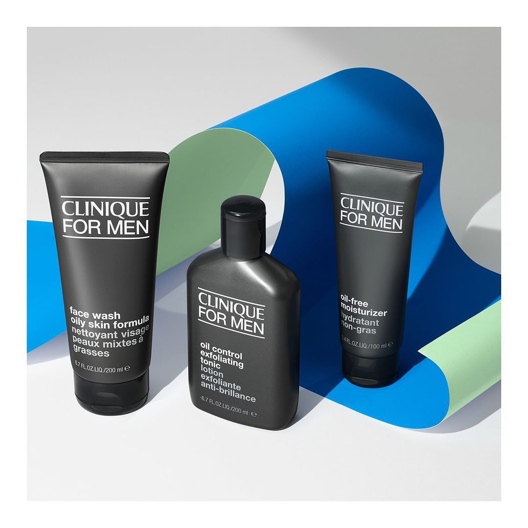 Three black Clinique for Men skincare product bottles, including face wash, toner, and moisturizer, displayed against a blue and green backdrop.