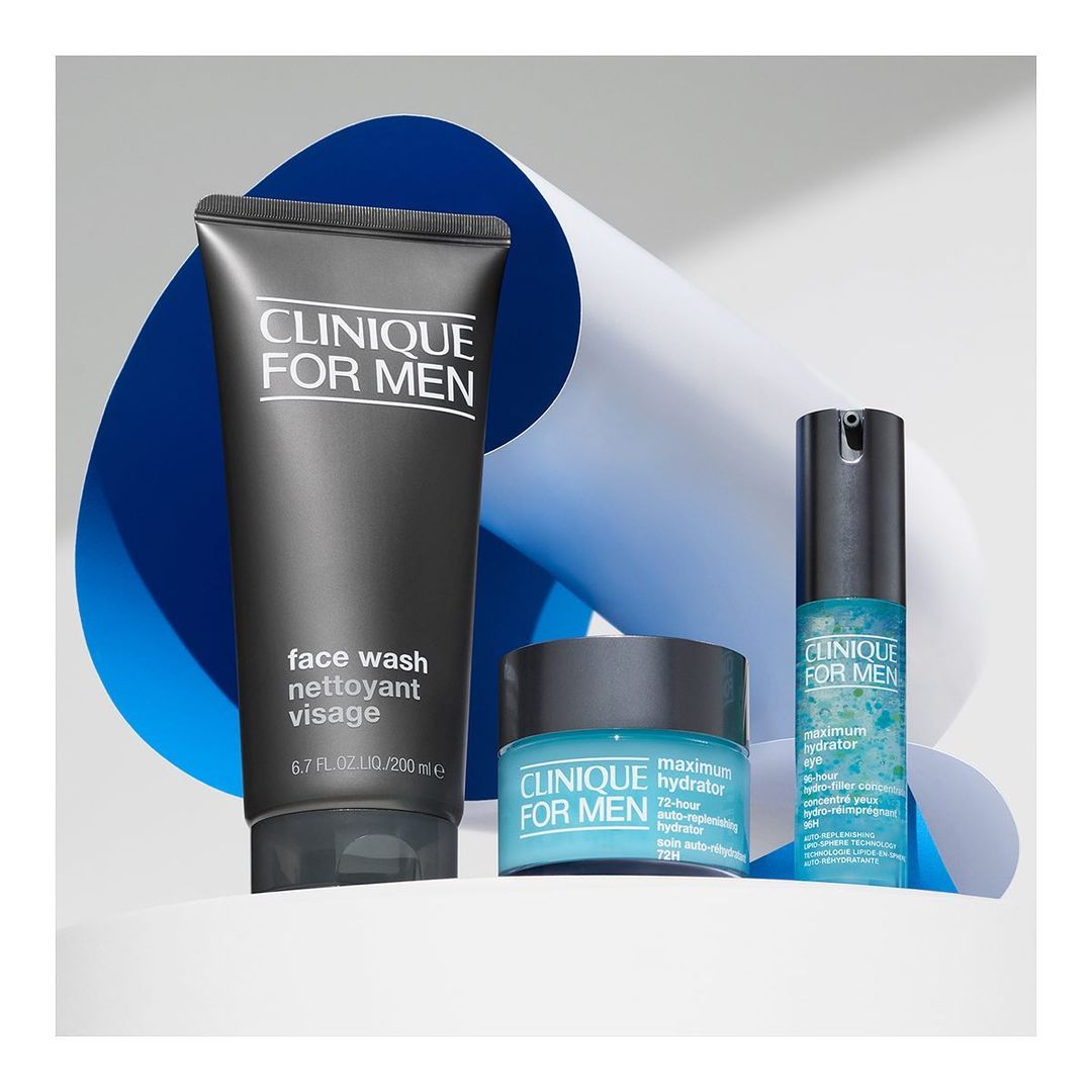 Three Clinique for Men skincare products sit on a white platform against a backdrop of blue and white curved paper.