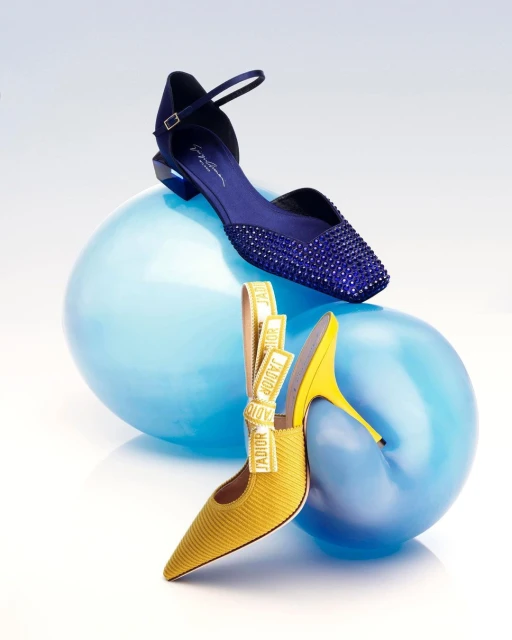 Two high heel shoes in yellow and blue are displayed on top of light blue balloons against a gradient white and blue background.