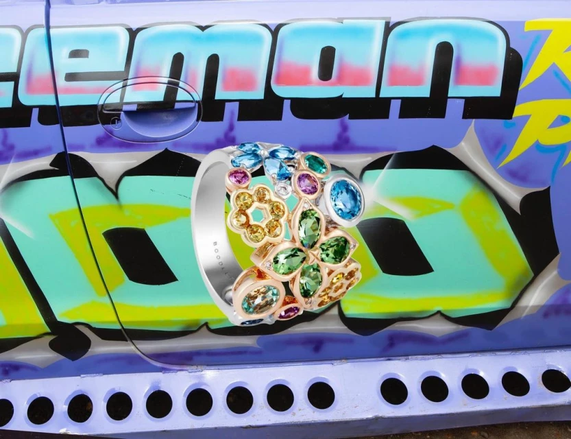Close-up of a gemstone-encrusted ring on a graffiti-covered surface, featuring colorful spray-painted letters and a playful, urban aesthetic.