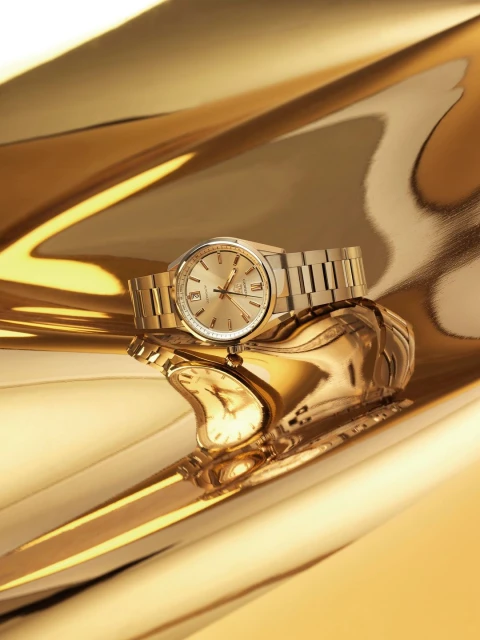 Close-up studio shot of an elegant gold wristwatch with a metal bracelet on a reflective gold surface, showcasing luxury timekeeping.